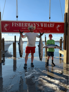 Father and son standing side-by-side holding fish after a fishing charter at Port Aransas.